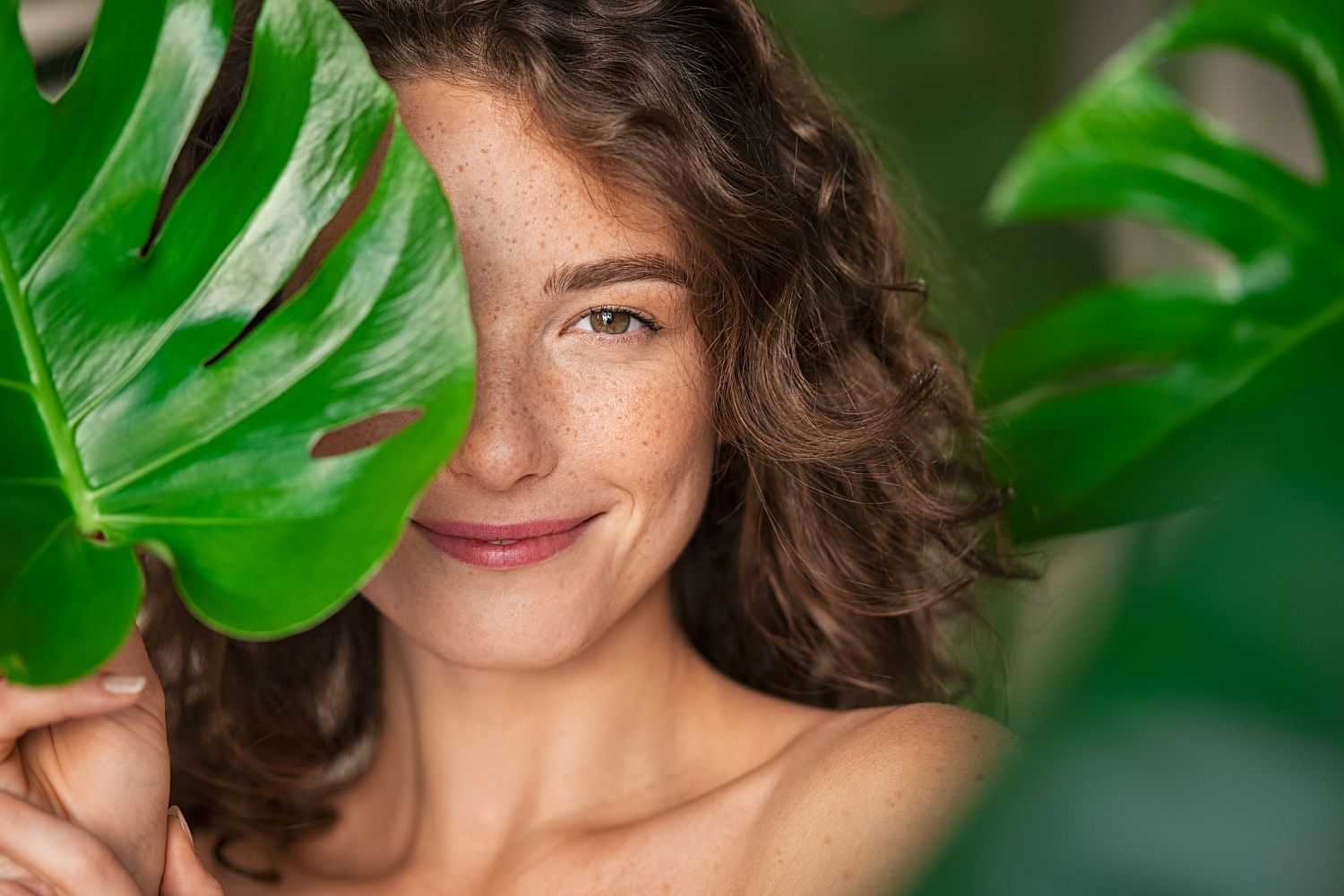 Woman smiling through large green leaves.